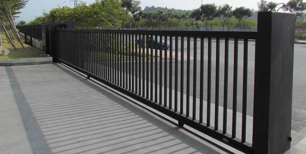 A black sliding steel fence are used to control access to a factory.